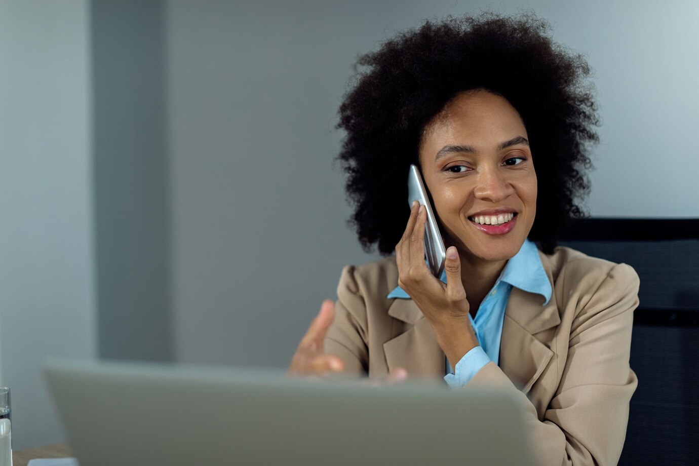 happy-black-businesswoman-taking-phone-while-working-laptop-office_637285-12951